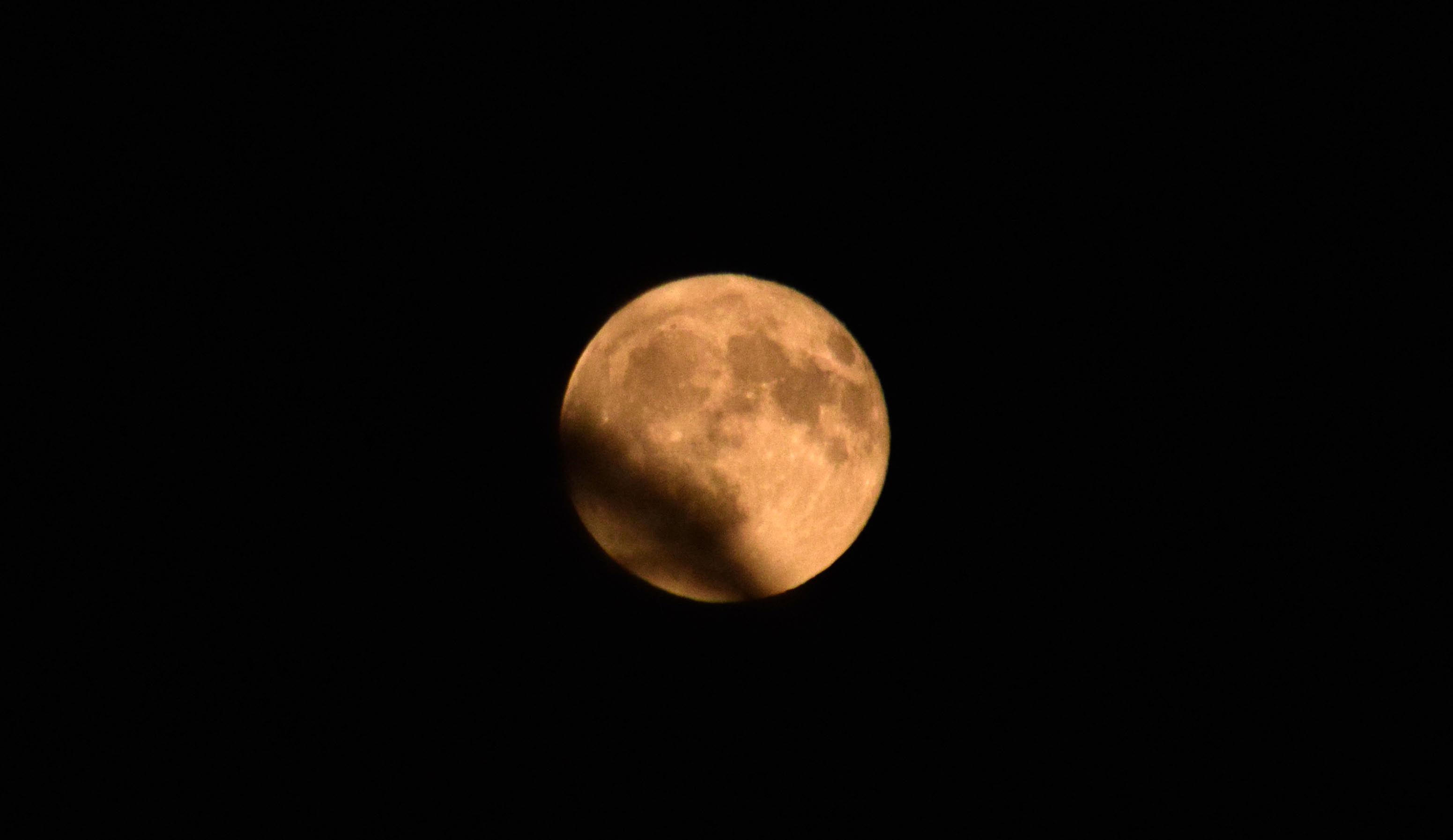 Fotografia di una Luna piena arancione oscurata per un quarto. 